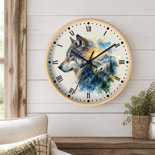 A round wall clock with a light wood frame hangs on a white shiplap wall above a wooden table. The clock face features a detailed watercolor illustration of a gray wolf over blue and green mountains and pine trees, with black Roman numerals and hands.