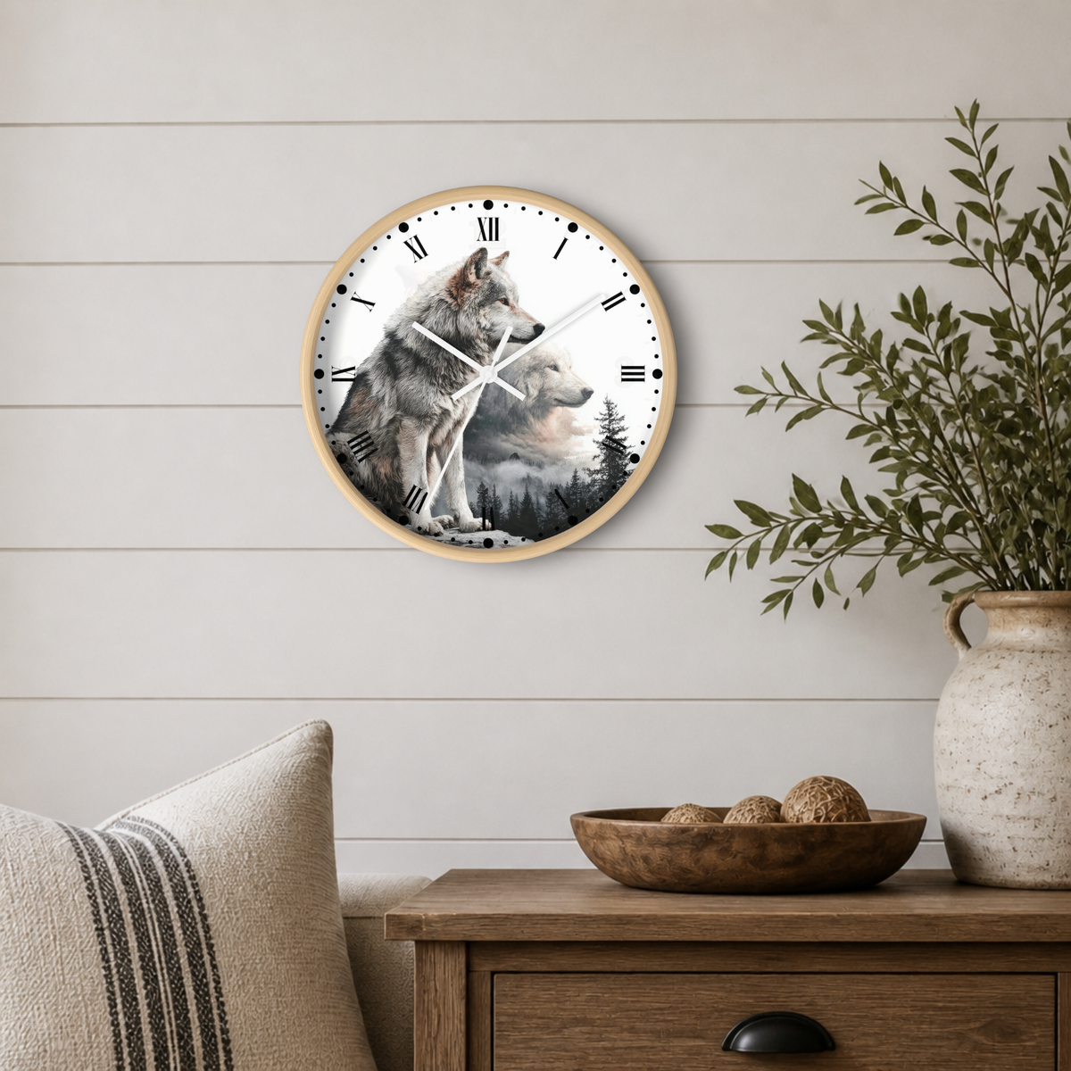 A round wall clock with a wolf illustration on the face, mounted on a white shiplap wall above a wooden side table with a plant and decorative bowl.
