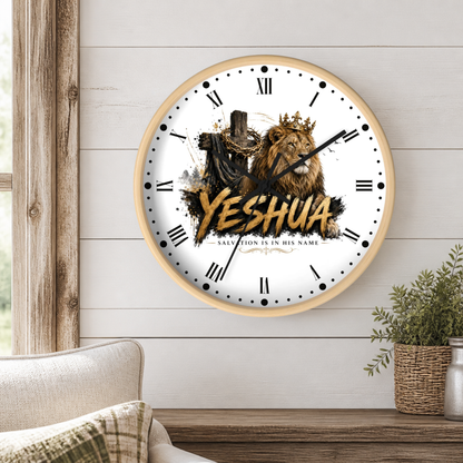 A round wall clock with a light wood frame hangs on a white shiplap wall above a wooden table. The clock face is white with black Roman numerals, black hands, and a graphic featuring a lion, a cross, and the word 'Yeshua' in large gold letters.
