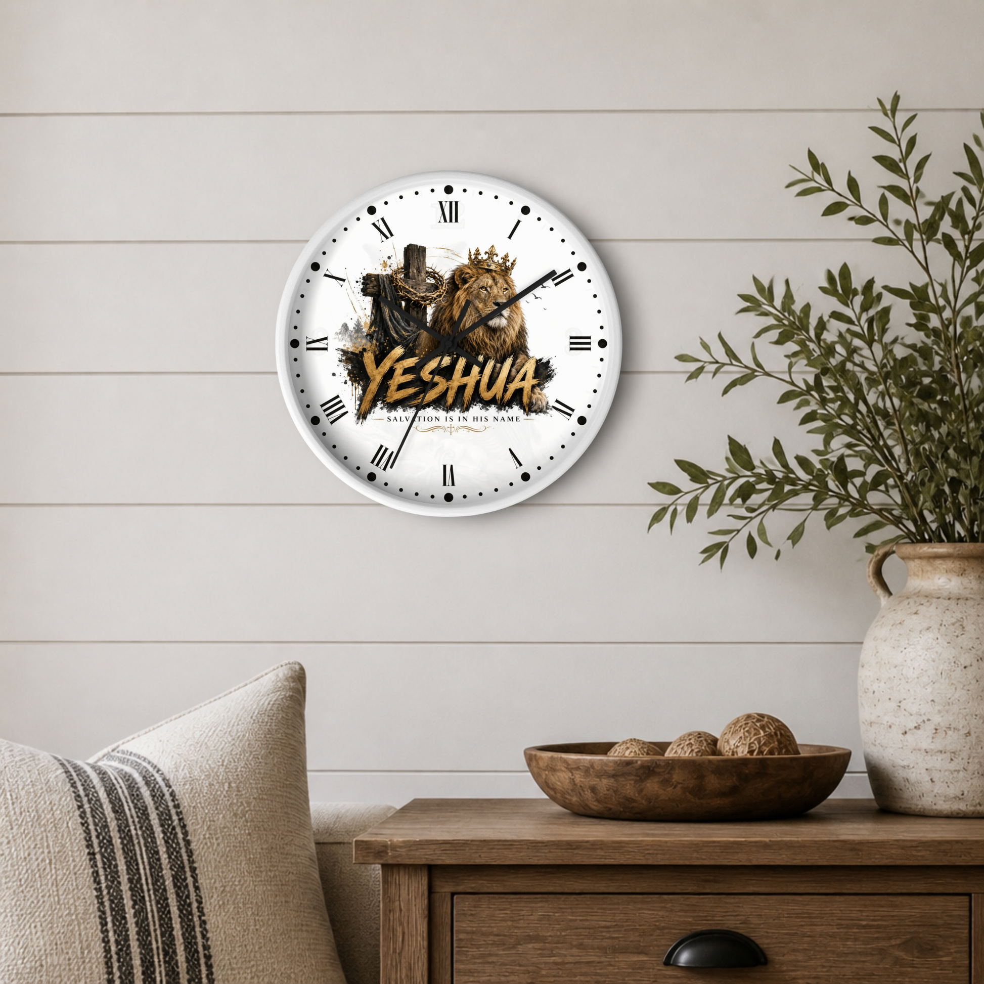 A round wall clock with Roman numerals and a graphic of Jesus and a lion, featuring the text 'YESHUA' in gold, mounted on a light wood paneled wall above a wooden side table with a plant and decorative bowl.