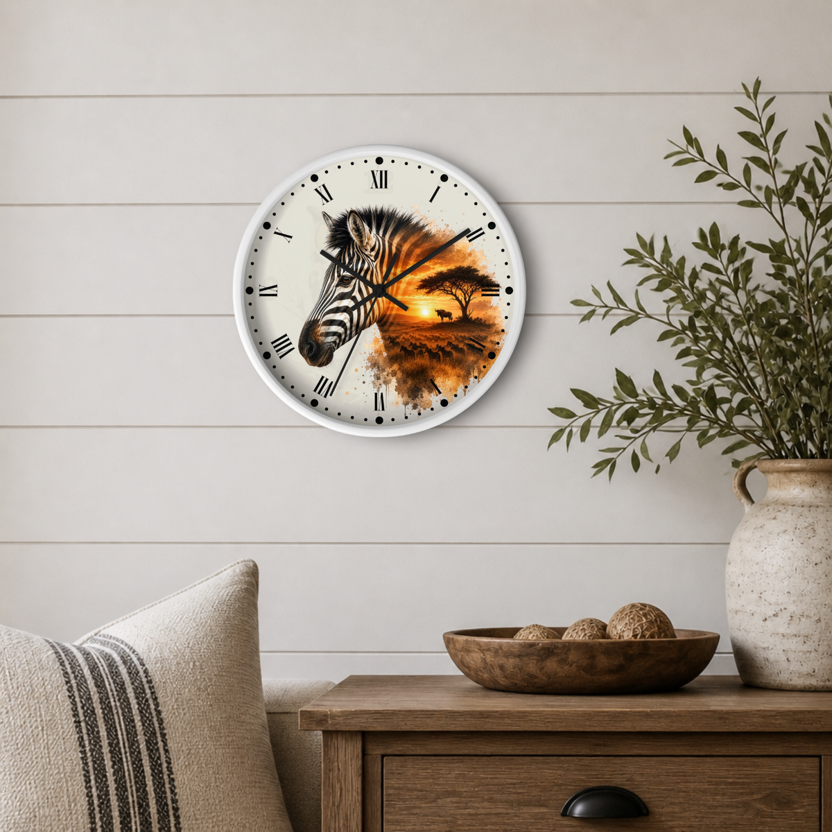 A round wall clock with a zebra and sunset landscape design, mounted on a light wood paneled wall above a wooden side table with a plant and decorative bowl.